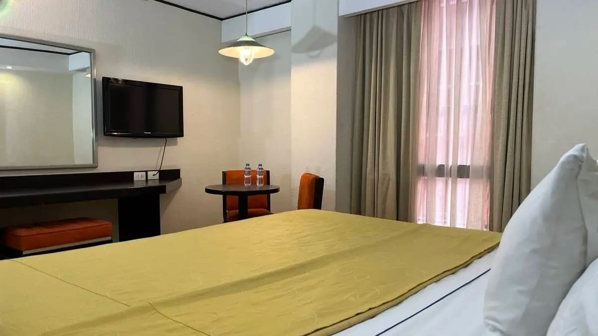 Habitación Suite Estándar con cama king size con una mesa con dos sillas y una televisión en la pared.